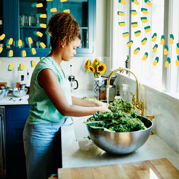 A woman washing leafy green vegetables in her kitchen sink