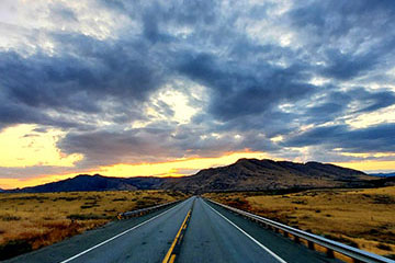 An open road with cloudy skies and mountains in the distance