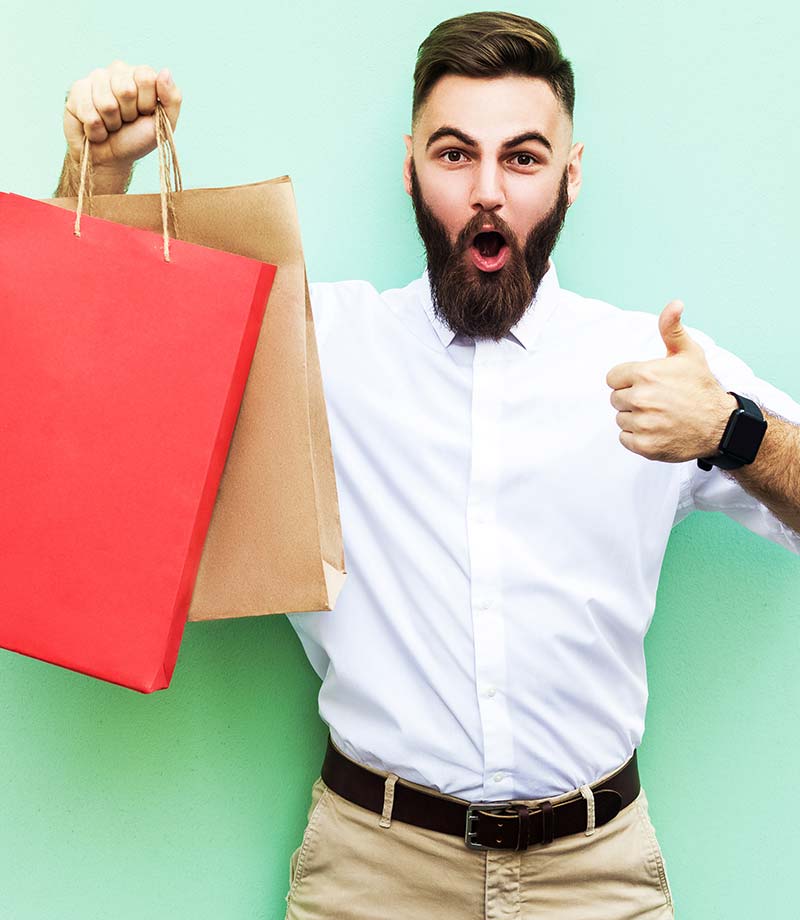 Young man excitedly holds up shopping bags and a thumbs up