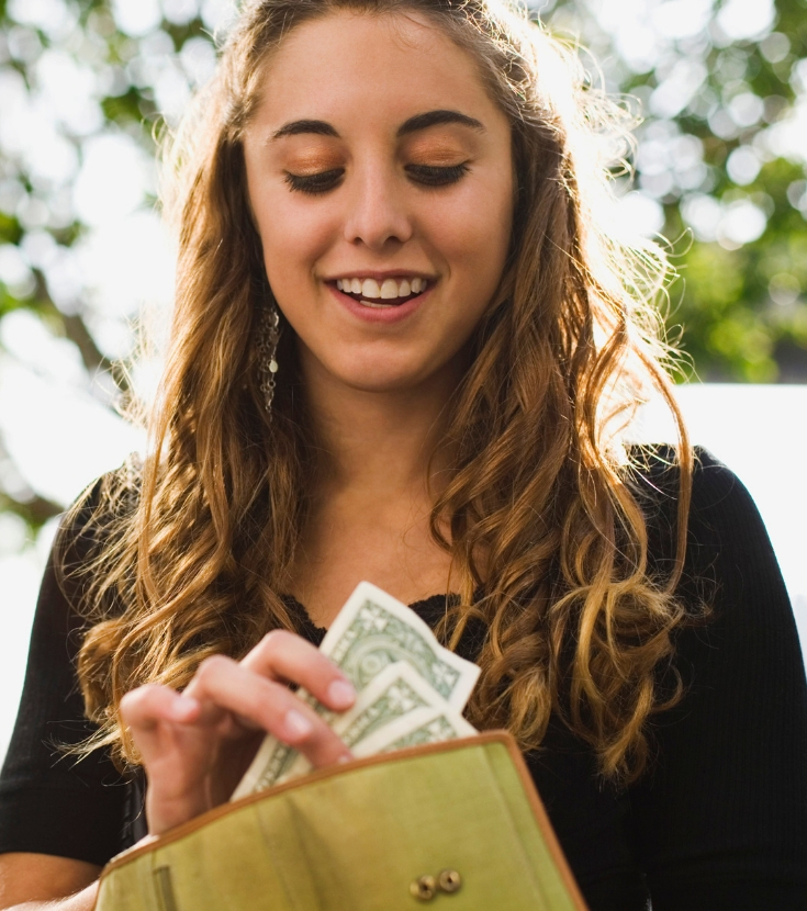 Woman smiling while taking dollar bills from her wallet