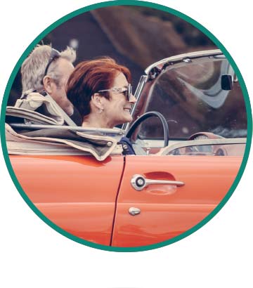 A couple in their 60s ride in a red convertible