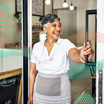 a barista goes to open a door to a coffee shop from the inside while wearing an apron