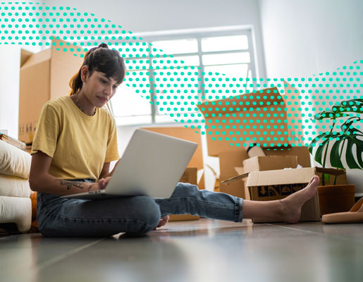 woman on working on a laptop, sitting on the floor surrounded by moving boxes