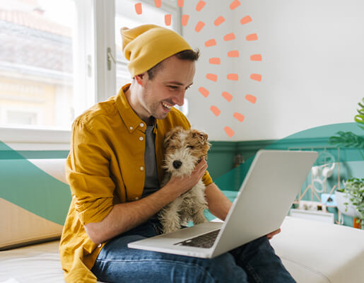 A man holding a dog, looking at a laptop screen, smiling