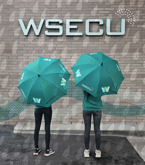 Two people standing in front of a wall, holding WSECU umbrellas