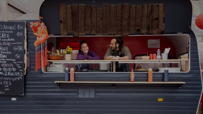 A woman and man leaning on the counter of a food truck, smiling