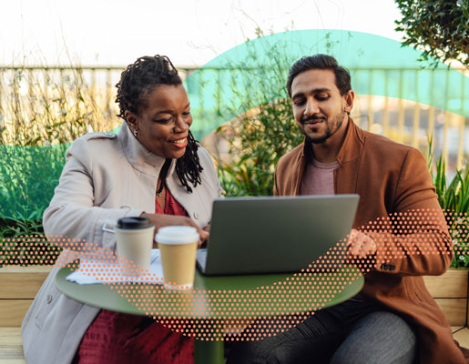 two people are sitting at a table looking at a laptop together and talking