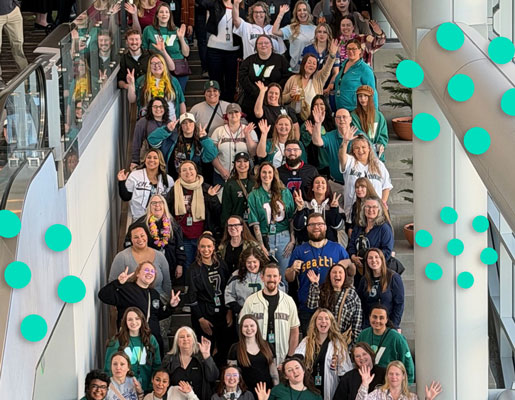 Crowd of people arranged on an escalator and staircase, smiling and waving toward the camera.