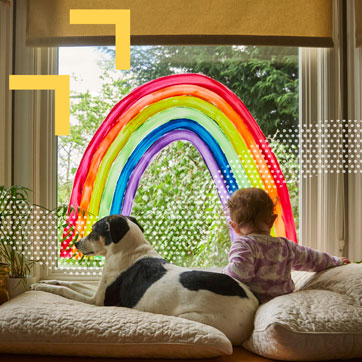 A dog and a baby sitting together while looking out a window with a rainbow painted on it
