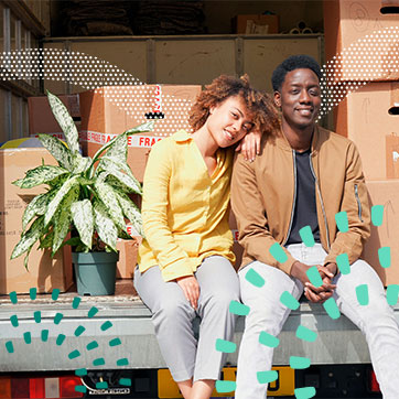 Couple sitting on the back of a moving truck with boxes behind them