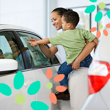 Mother carrying a child while pointing at a car's information sheet