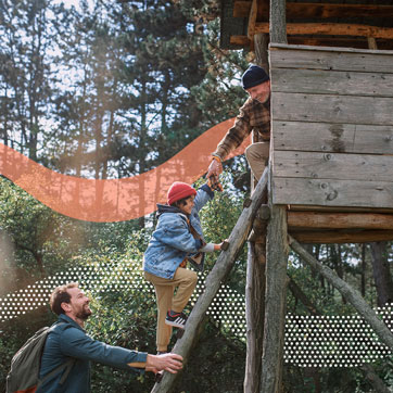 A boy climbing a tree house with his father and grandfather