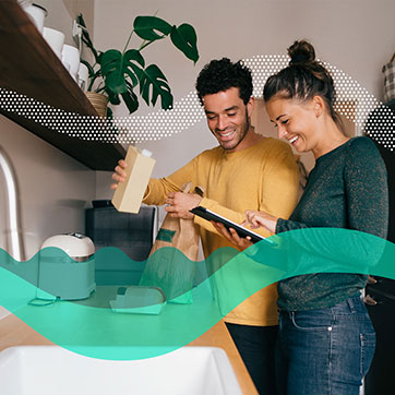 A couple in the kitchen happily looking at a tablet computer while putting away groceries