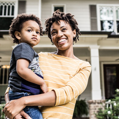 woman holding child and standing in front of a house