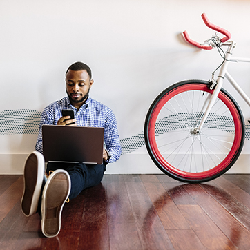 man with a phone and computer sitting next to a bicycle