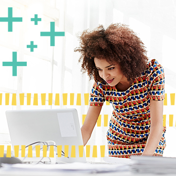 Curly haired woman looking at a laptop while standing