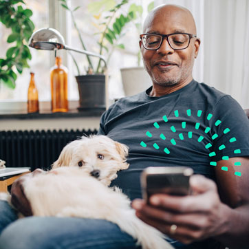 A man sitting down with a dog on his lap, looking at a cellphone