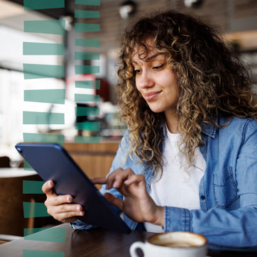 A woman sitting on a cafe booth, tapping on a tablet screen