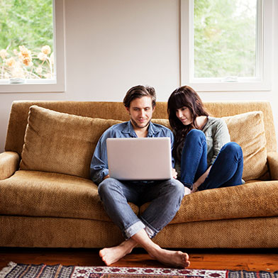 a couple sitting on a couch looking at a laptop
