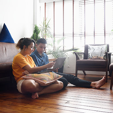 a couple sitting on their living room floor pointing something out on a laptop