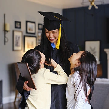 A woman in a graduation cap and gown, hugging her kids