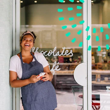 A woman standing outside of a storefront, holding a cell phone