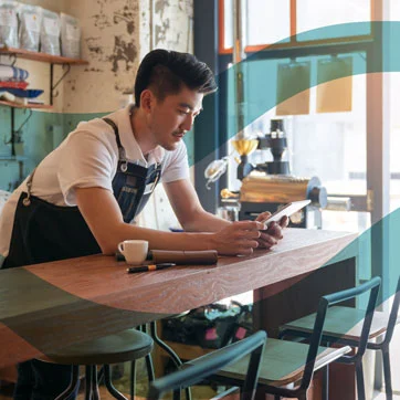 A man holding a cell phone, standing at a coffee bar