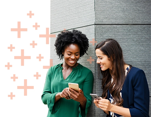 Two women looking at their cellphones, smiling.