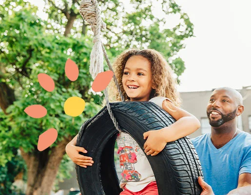 A father playing with his child sitting on a tire swing.